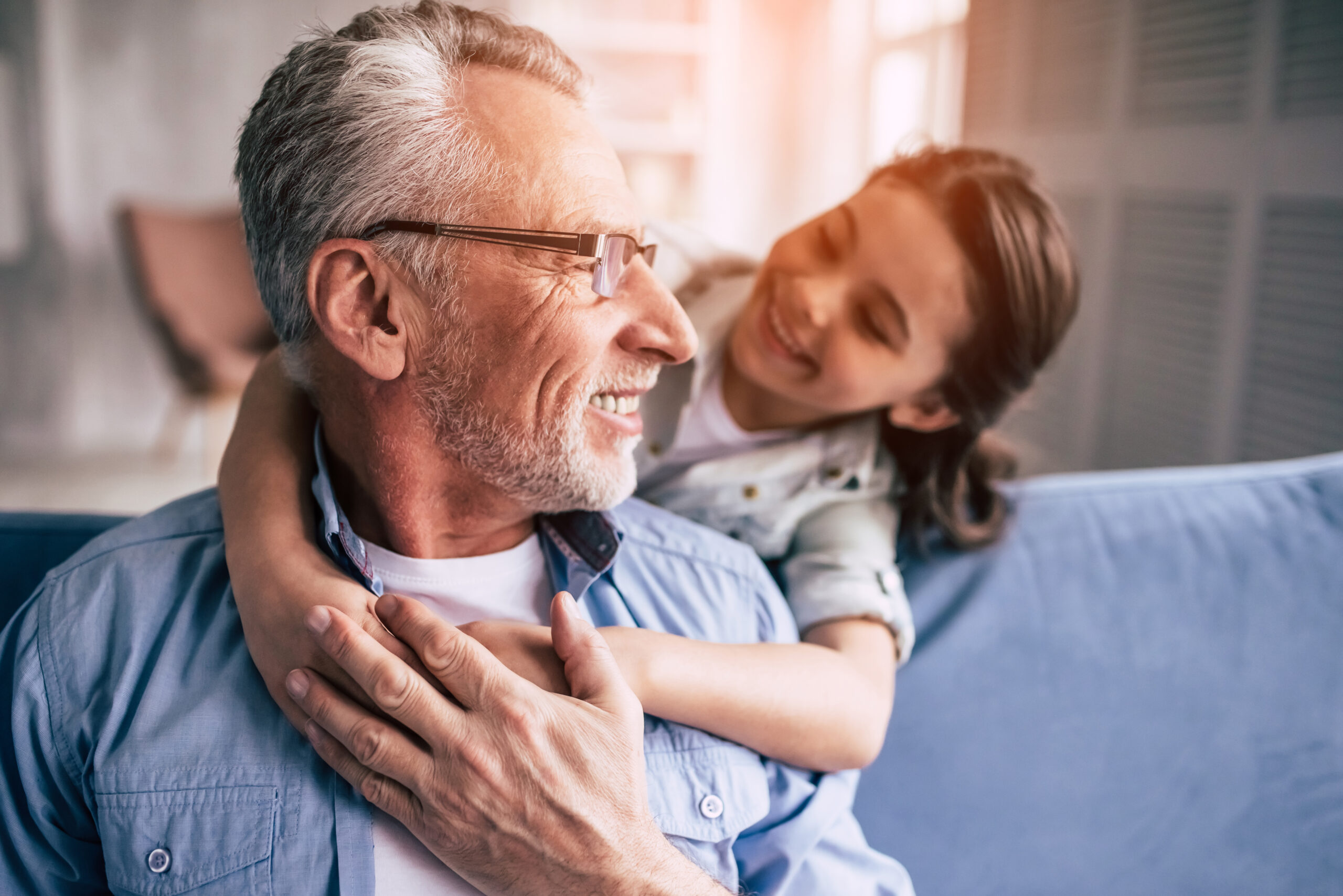 The happy girl hugs a grandfather on the sofa